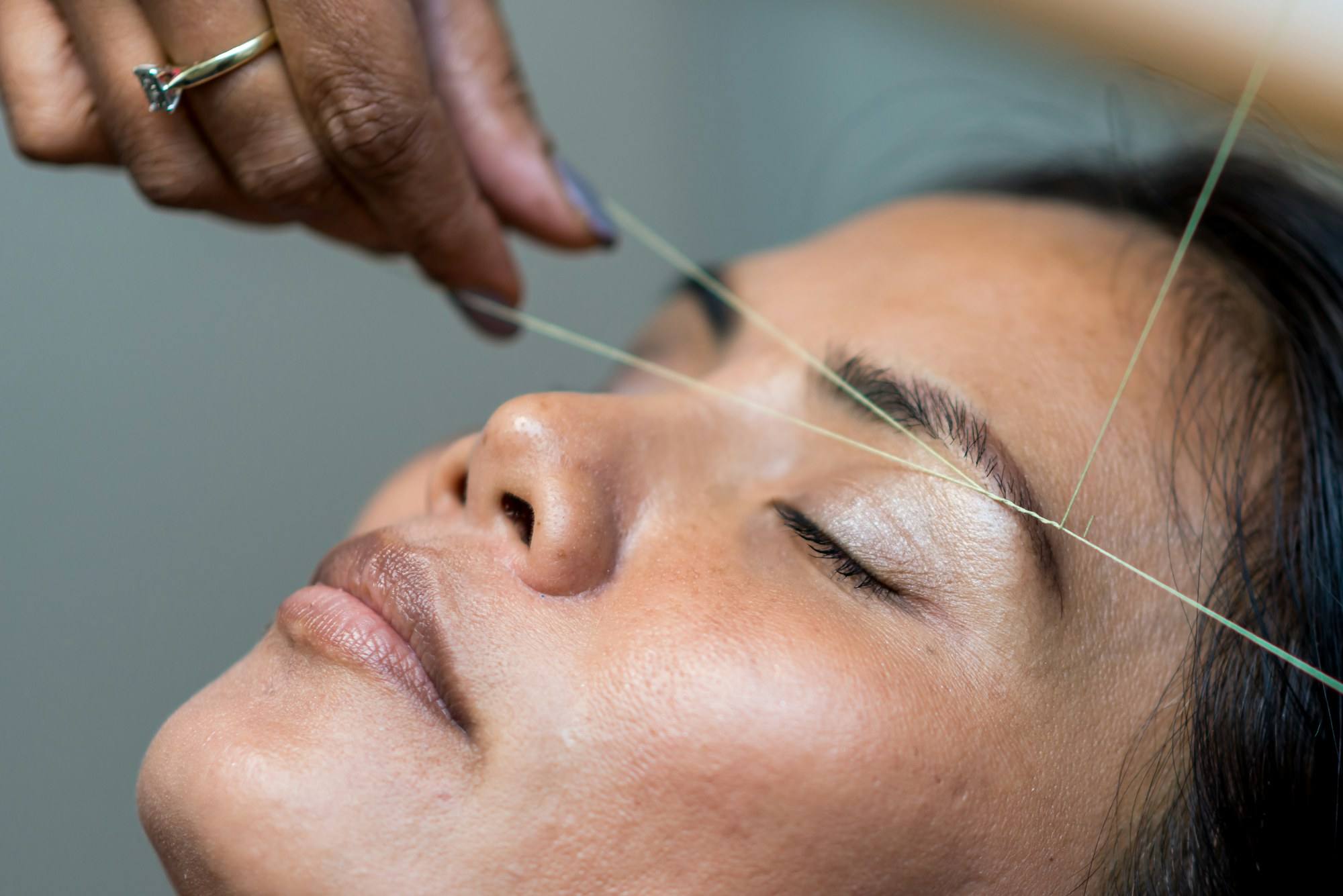 A brow being shaped with thread on a relaxed client with closed eyes