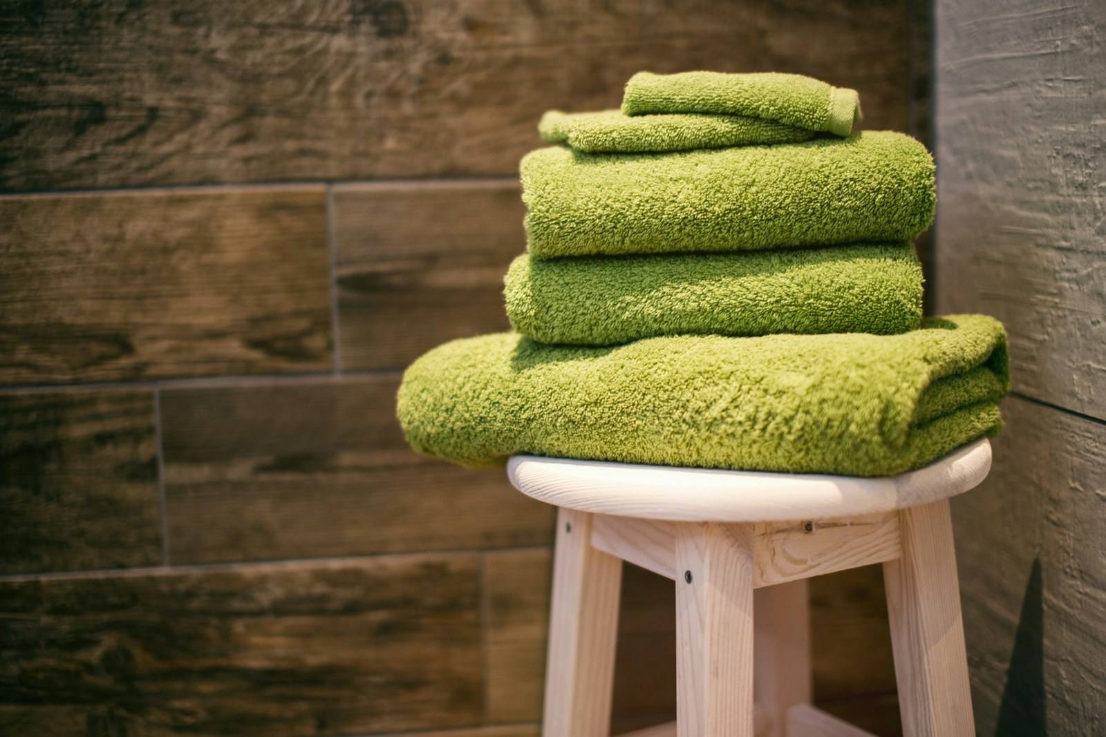 A stack of folded green towels on a small wooden stool
