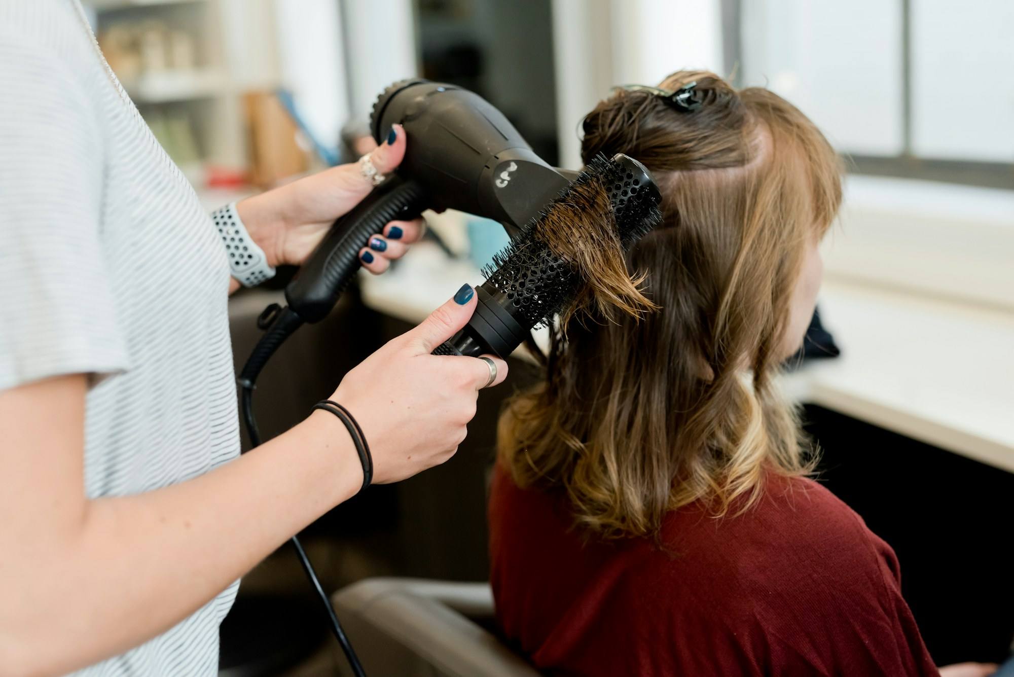 A hairstylist using a blow dryer and round brush on a client’s long hair