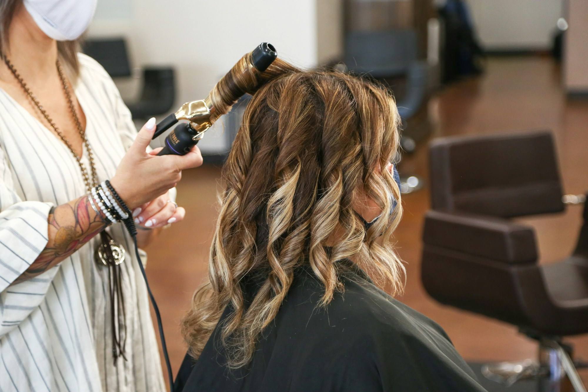 A stylist shaping long wavy hair with a curling iron in a bright salon