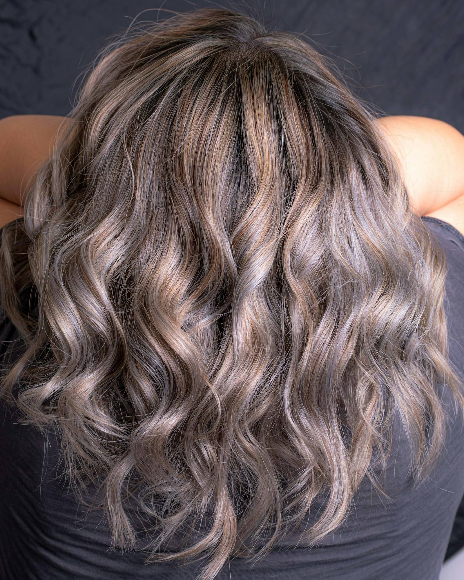 The back of a shoulder-length head of hair in soft waves with cool ash and brown tones