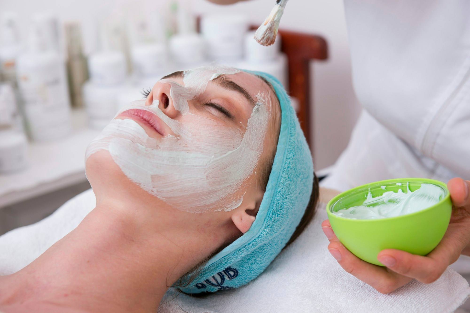 A woman lying back on a blue towel with a cream mask across her face