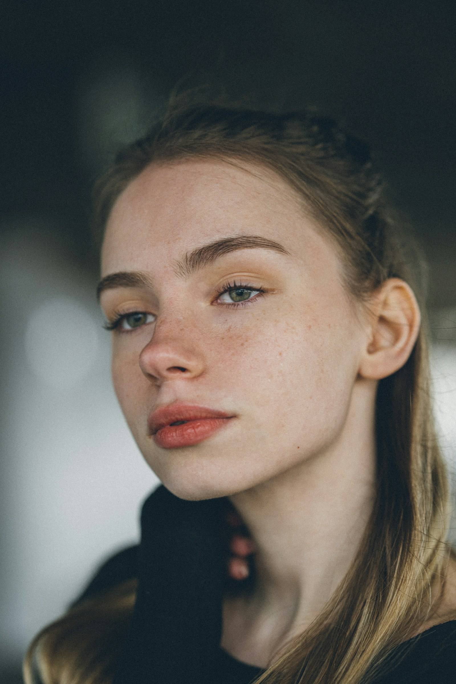 Young woman with freckles and hair pulled back, looking toward the camera (illustrative photograph)