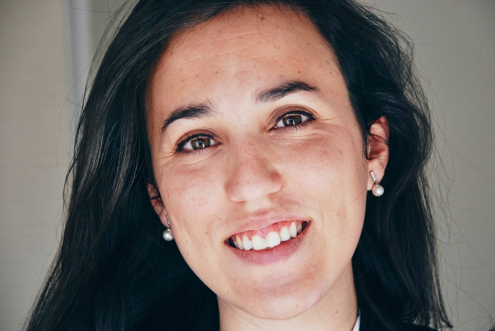 Smiling woman with long dark hair and pearl earrings, photographed close up (illustrative photograph)