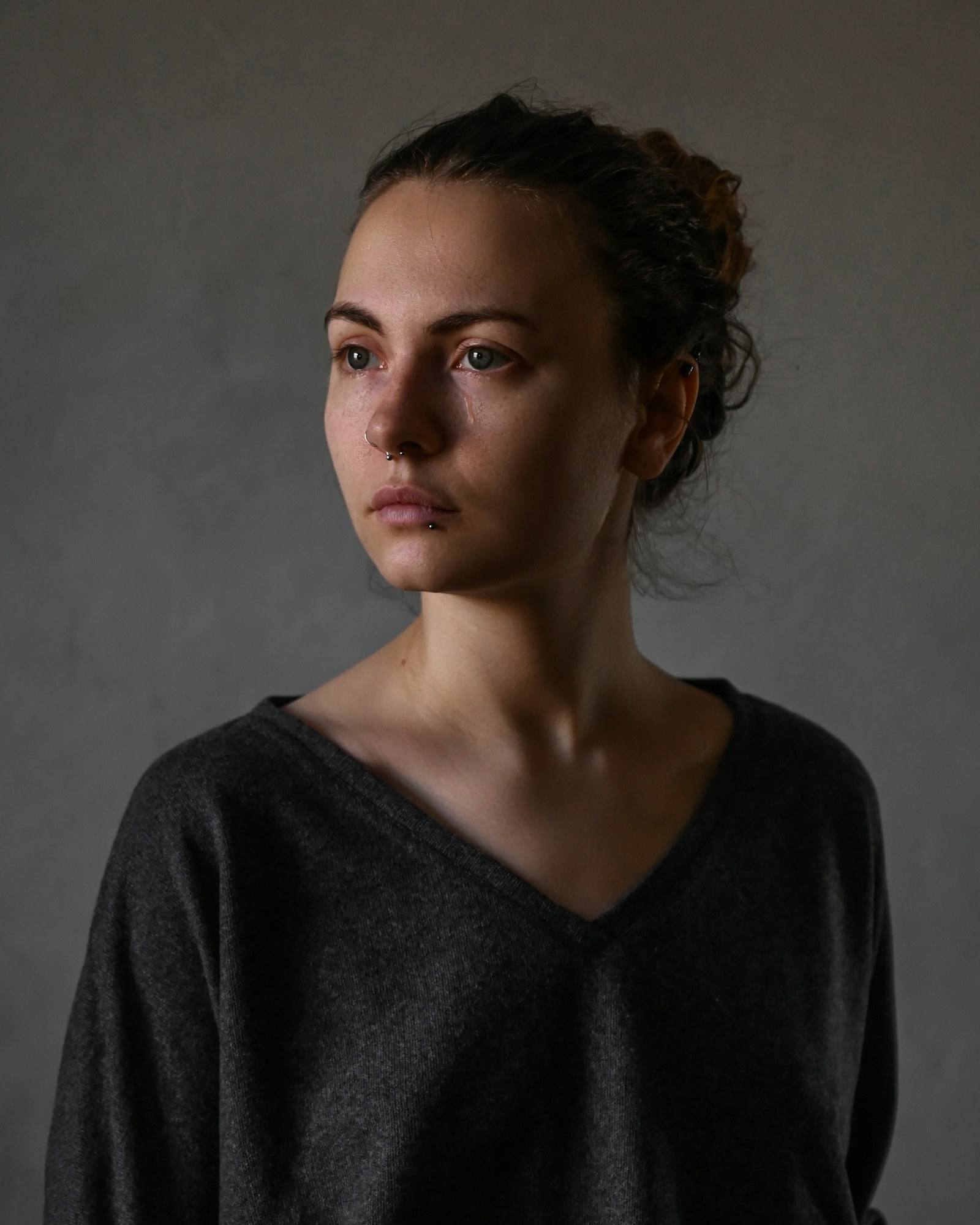 Woman in a dark sweater looking to the side in soft window light (illustrative photograph)